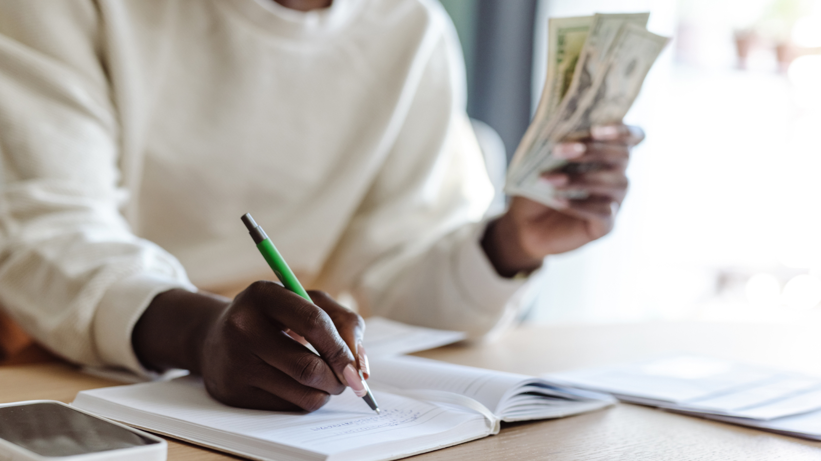 With cash in hand, a person plans their finances by writing in a notebook.
