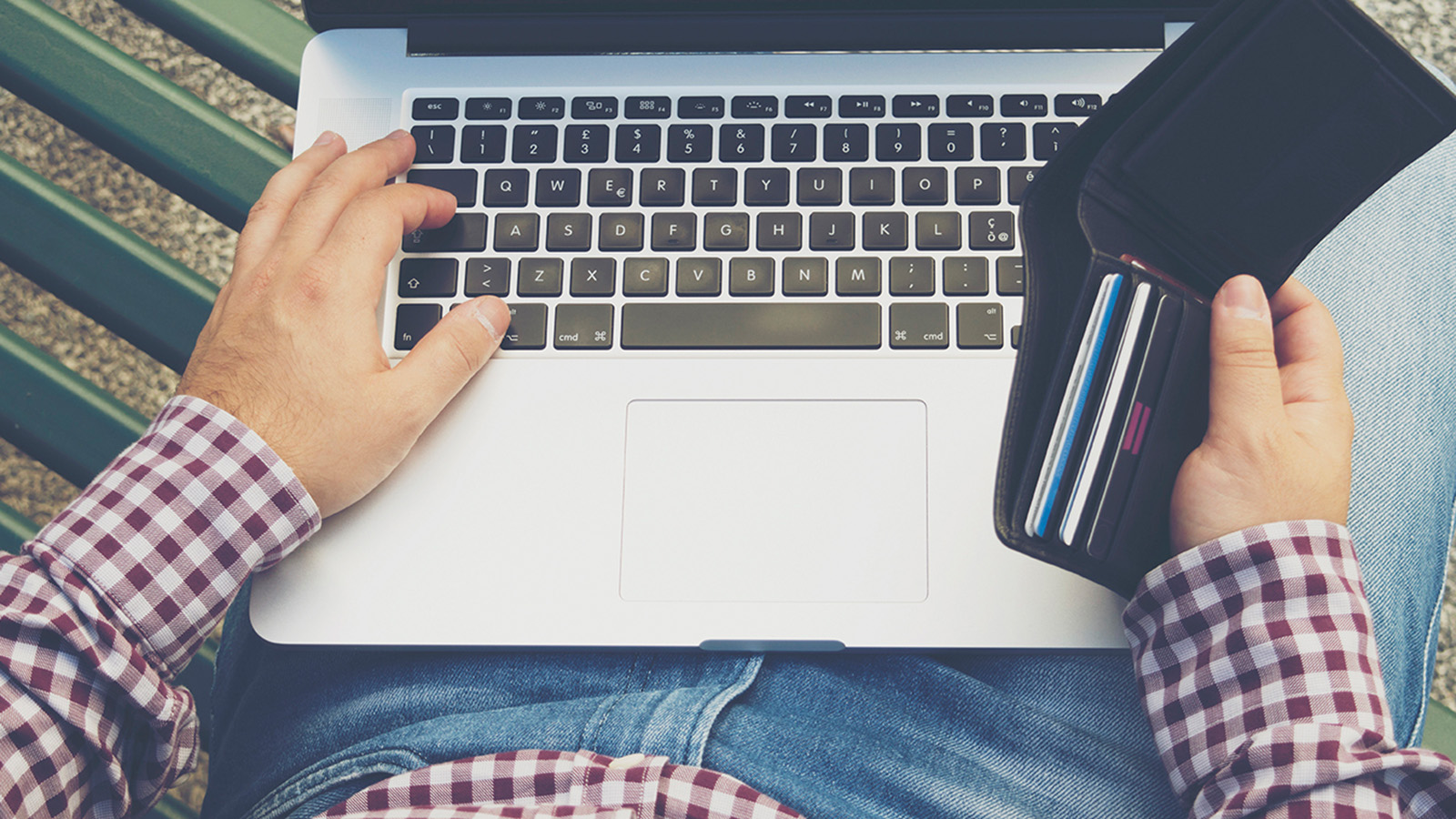 Customer sitting on a bench with a laptop and a wallet making an online payment.