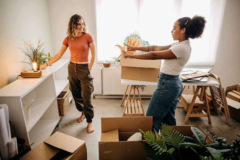 Two young women roommates unpacking moving boxes and organizing their new apartment, a common milestone when considering renters insurance.