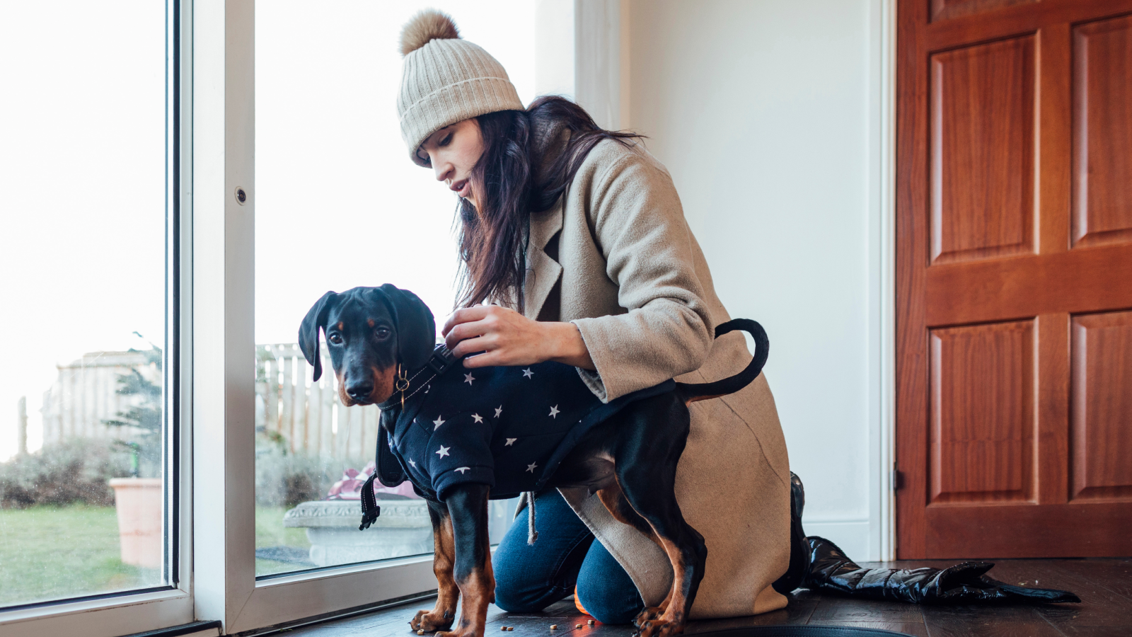 Woman in winter clothes with a puppy in a sweater getting ready for a walk.