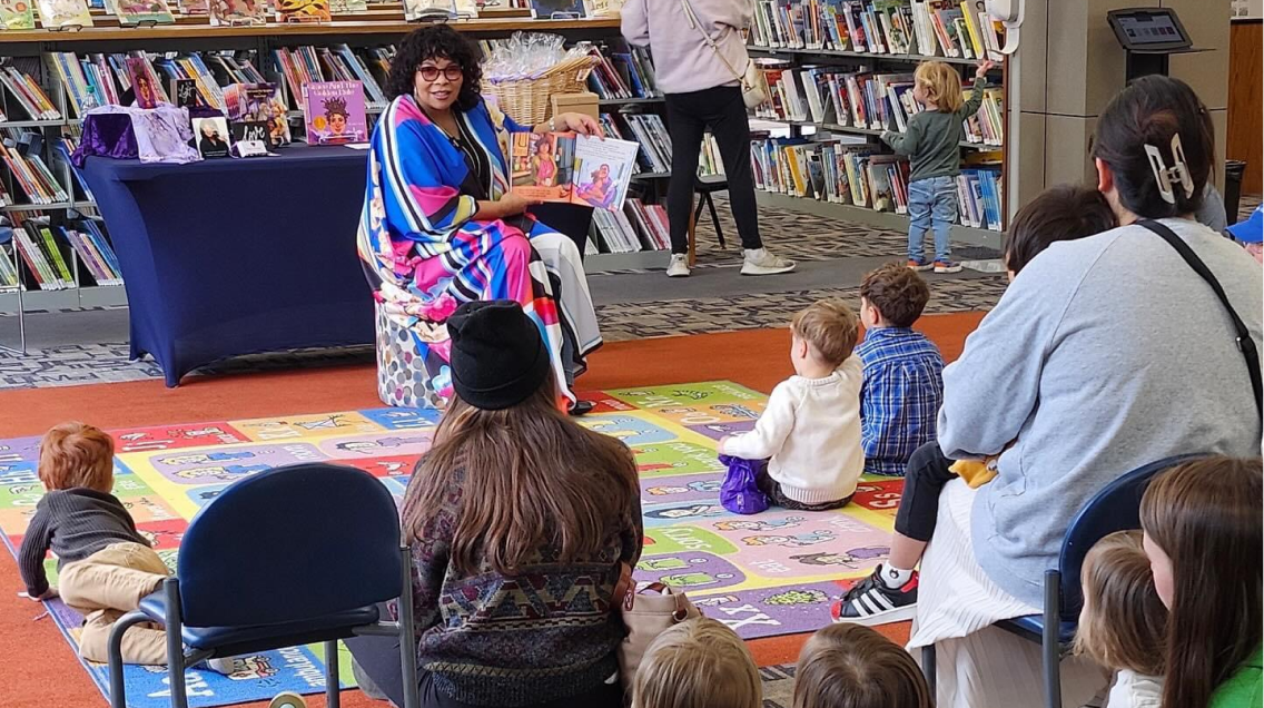 Negrita Smart reading her book in front of children and adults in a library.