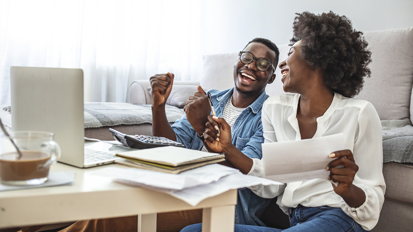 A man and woman at a table with a computer and papers laughing together.
