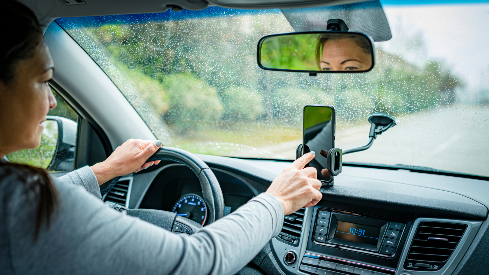 A woman touches the screen of a car-mounted smartphone while driving.