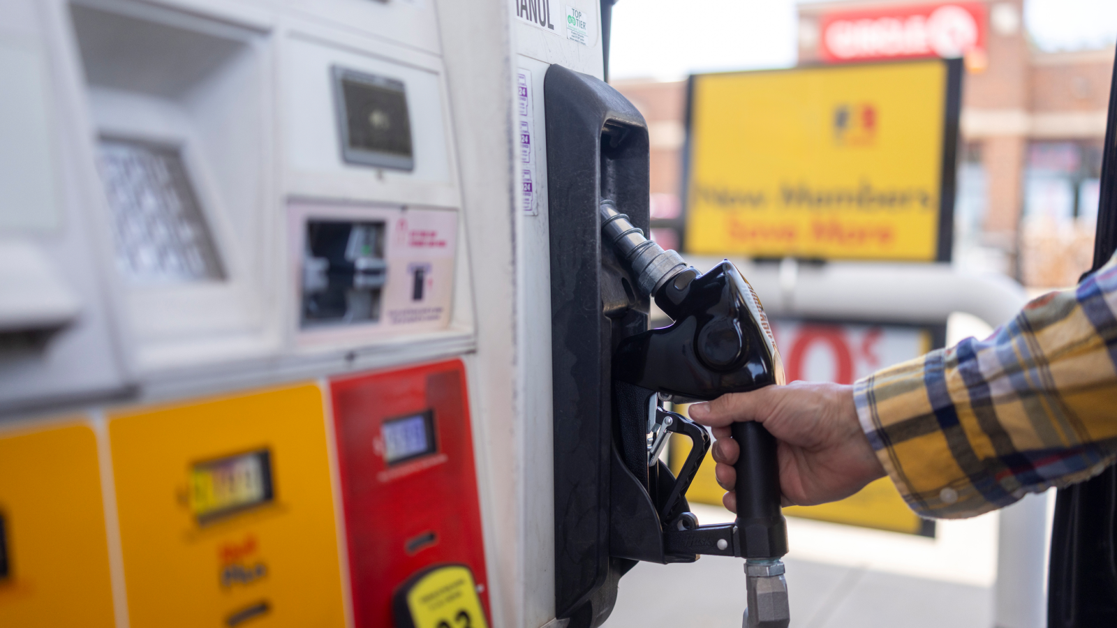 A driver choosing between gasoline options at the pump before fueling their car.