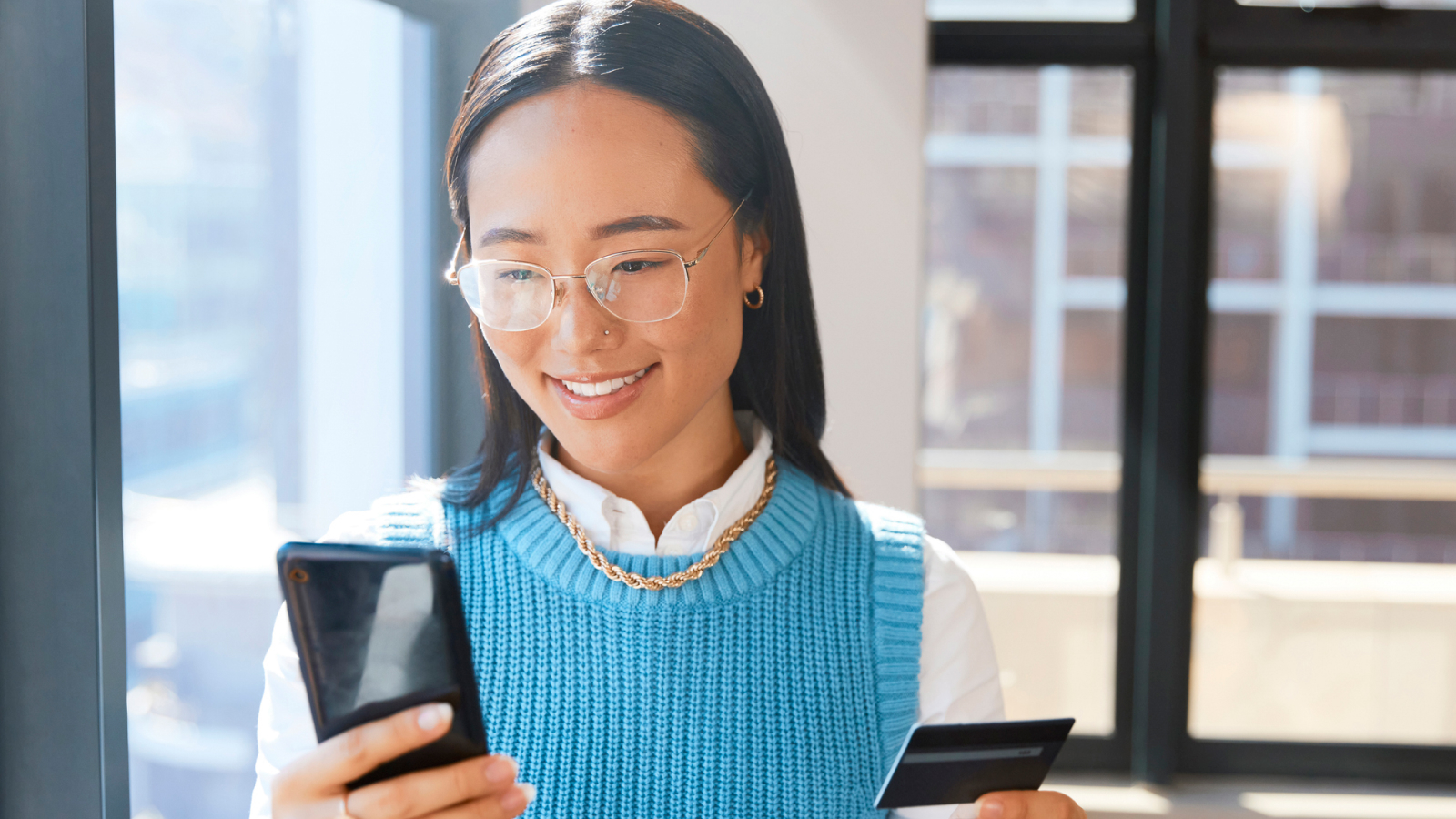 Woman looking at phone and holding a credit card.