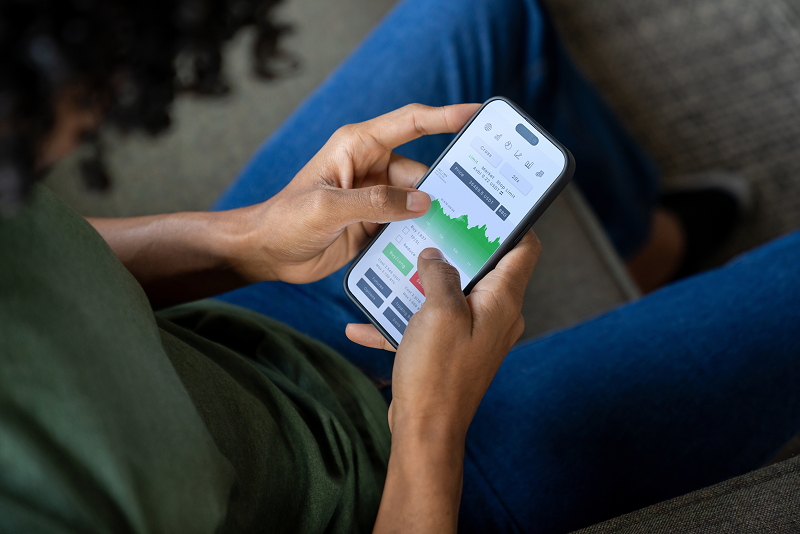 Close-up of a person reviewing cryptocurrency prices and a trading chart on a smartphone.