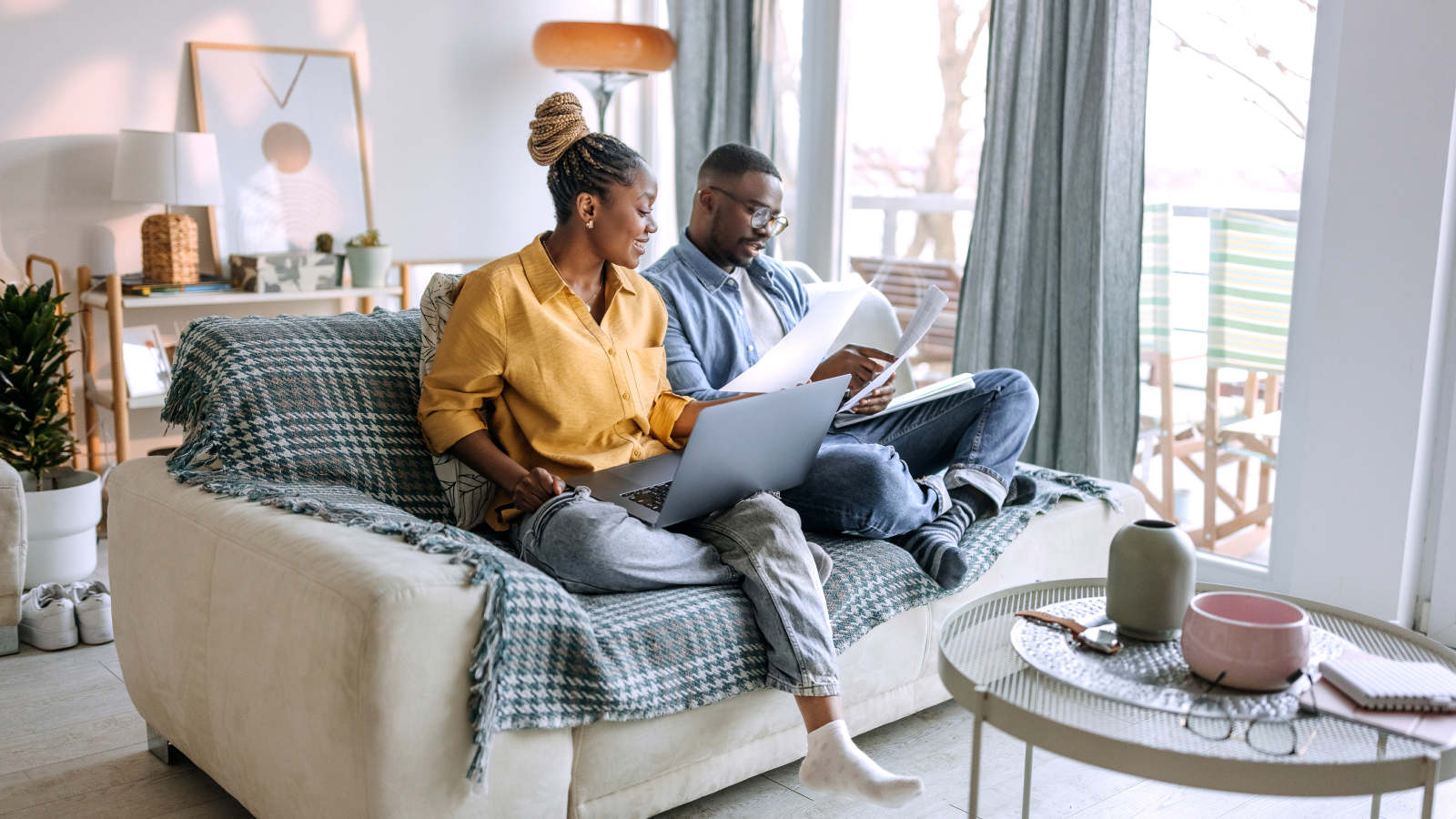 Couple on couch working on computer with paperwork.