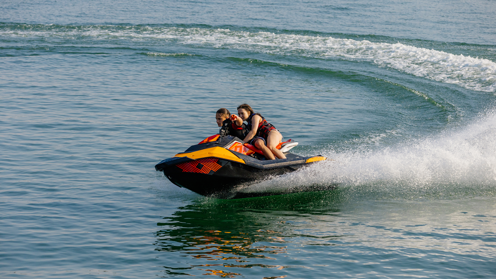 Two teenagers make a sharp turn while riding a jet ski in open water. 