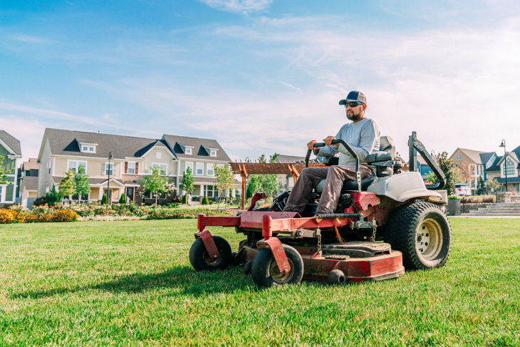 Man on a riding commercial lawnmower cutting a large back yard.