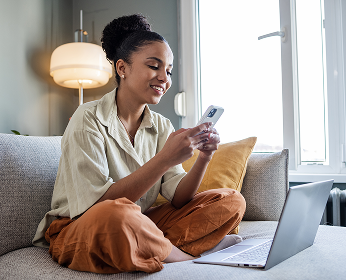 Woman looking at phone sitting in front of her laptop.