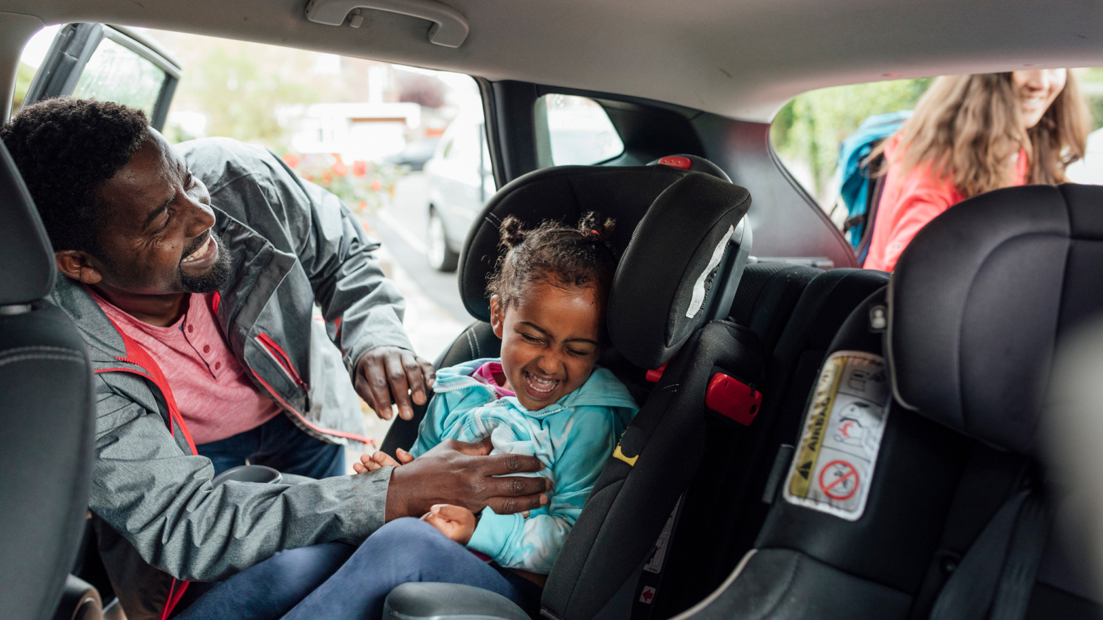 A picture of a man putting a child in their car seat.
