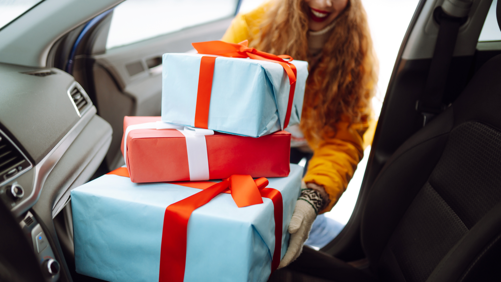Woman placing large Christmas presents into passenger side of vehicle. 