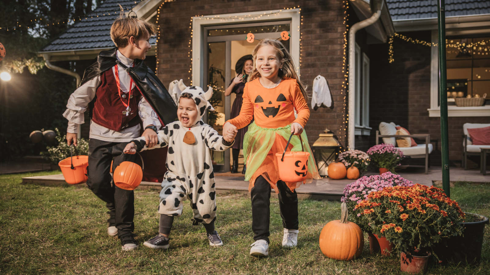 Excited, young trick-or-treaters holding hands leaving home with candy baskets. 