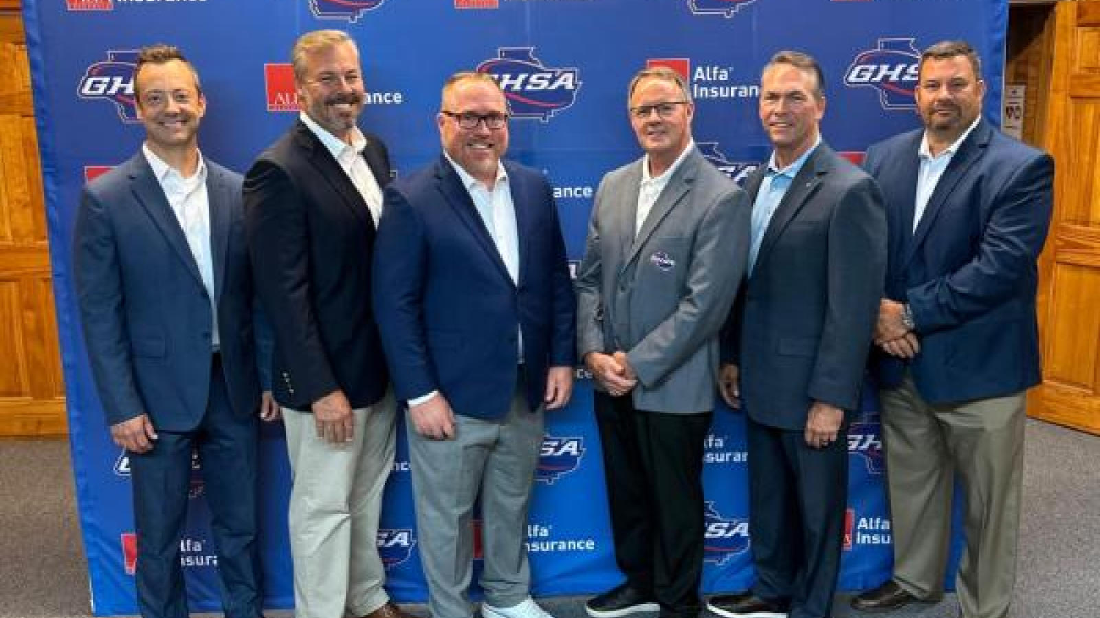 A picture of six men standing in front of a partnership backdrop with the GHSA.