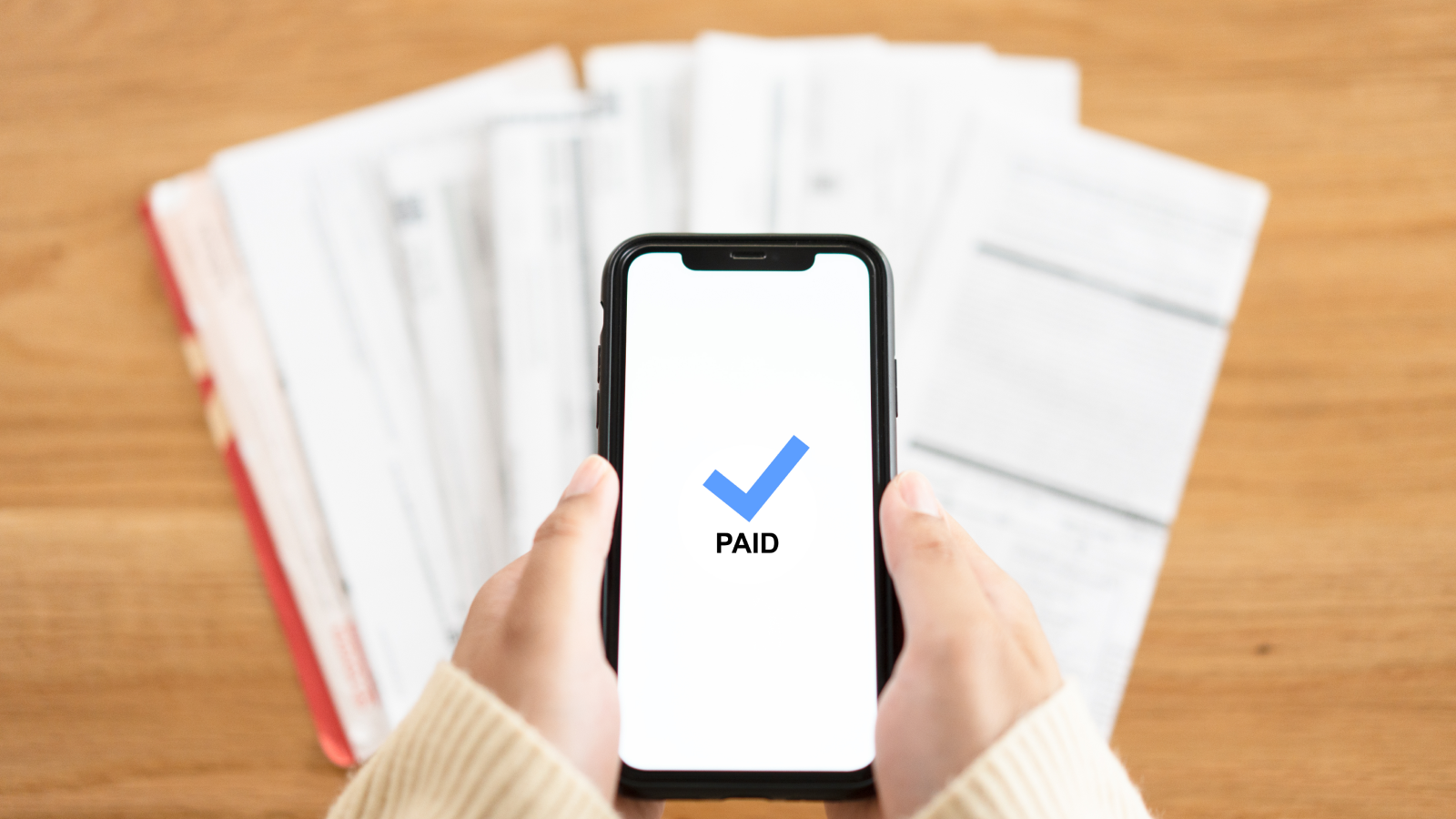 Person holding mobile phone after making a payment over paper invoices. 